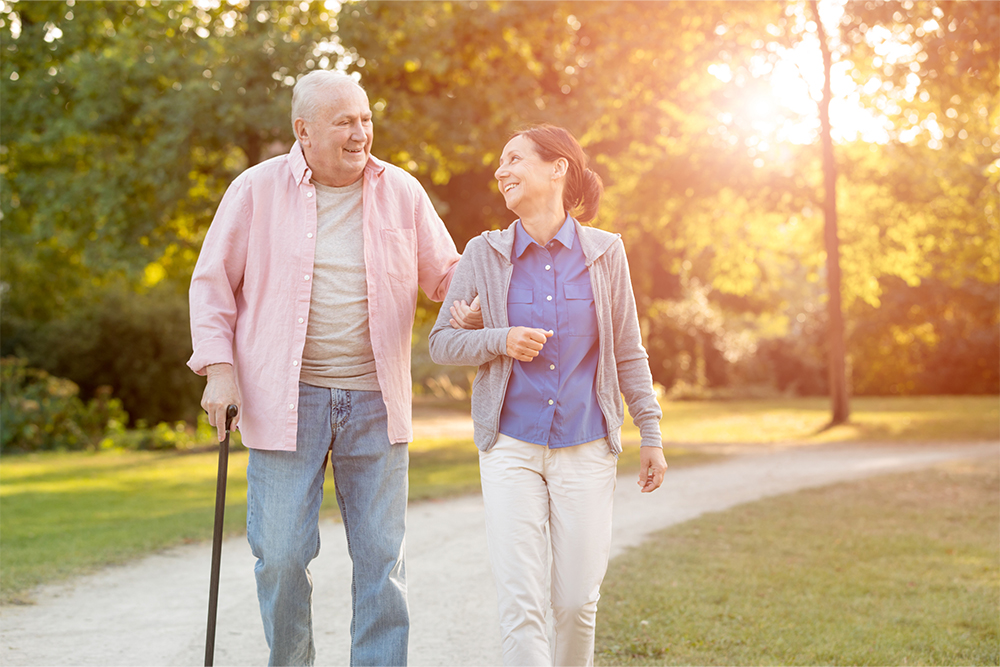 An older adult man walking with companion outside.