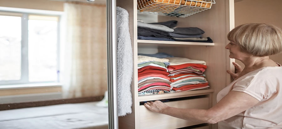 Senior woman choosing outfit from wardrobe closet with clothes and home stuff. Cleaning, organizing and order in the closet