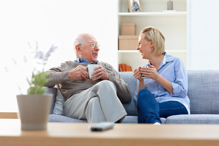 Senior man and female carer enjoying coffee in living room